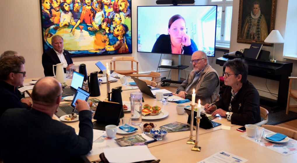 Dette billede viser  møde i det grønne stiftsudvalg, der sidder omkring et bord fyldt med dokumenter, bærbare computere og snacks. 