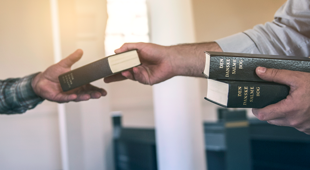 Hånd der giver salmebog til en anden